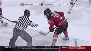 Hockey player in red jersey faces off against opponent as referee drops the puck during a game. Scoreboard displays Ohio State 0, Wisconsin 1