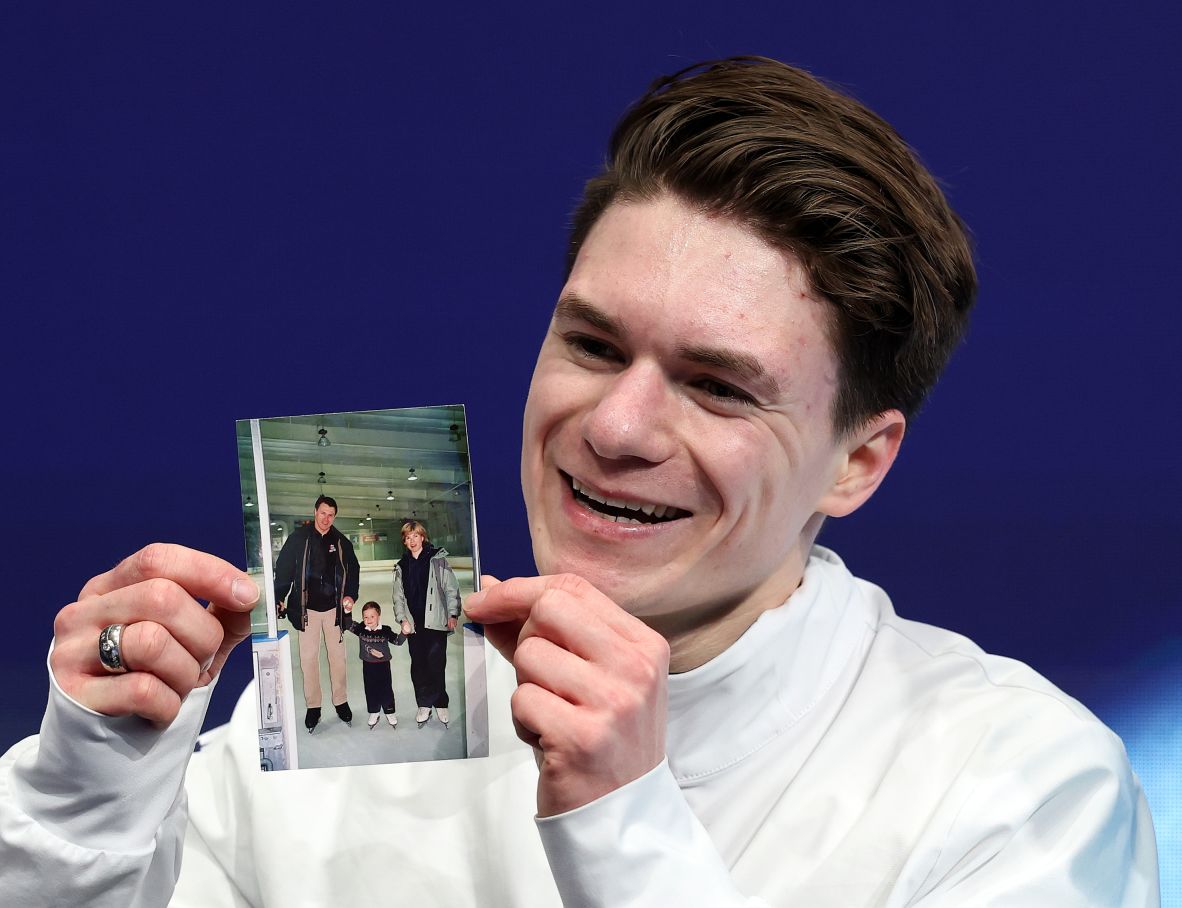 After competing in the short program on February 10, US figure skater Maxim Naumov holds up a picture of himself as a child with his parents. His parents and lifelong coaches — world champions Evgenia Shishkova and Vadim Naumov — <a href=