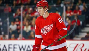 A concept visualization showing Winnipeg Jets defenseman Logan Stanley wearing a red Detroit Red Wings home jersey with number 64, red helmet, and gloves, standing on the ice holding his stick during a game.