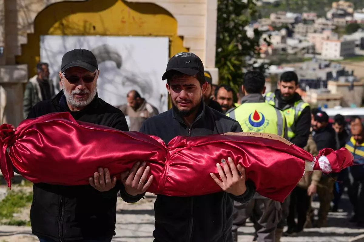 A man, left, carries the body of his son, Kassem Younis, who was killed in an Israeli airstrike, during his funeral procession in the southern village of Chehabiyeh, Lebanon, Wednesday, March 11, 2026. (AP Photo/Mohammed Zaatari)