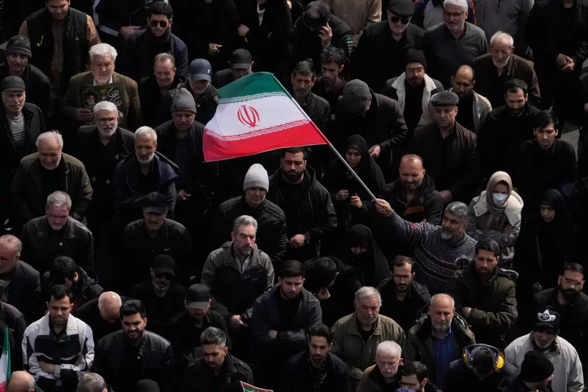 A man waves an Iranian flag as a crowd attends the funeral procession for senior Iranian military officials and civilians killed during the U.S.-Israel campaign in Tehran, Iran, Wednesday, March 11, 2026. (AP Photo/Vahid Salemi)