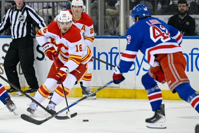 Mar 10, 2026; New York, New York, USA; Calgary Flames center Morgan Frost (16) skates with the puck defended by New York Rangers center Noah Laba (42) during the first period at Madison Square Garden.