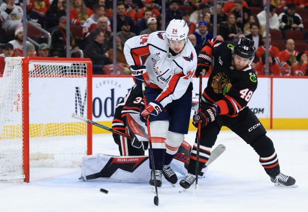 Capitals center Connor McMichael and Blackhawks defenseman Matt Grzelcyk reach for the puck Jan. 9, 2026, at the United Center. (John J. Kim/Chicago Tribune)