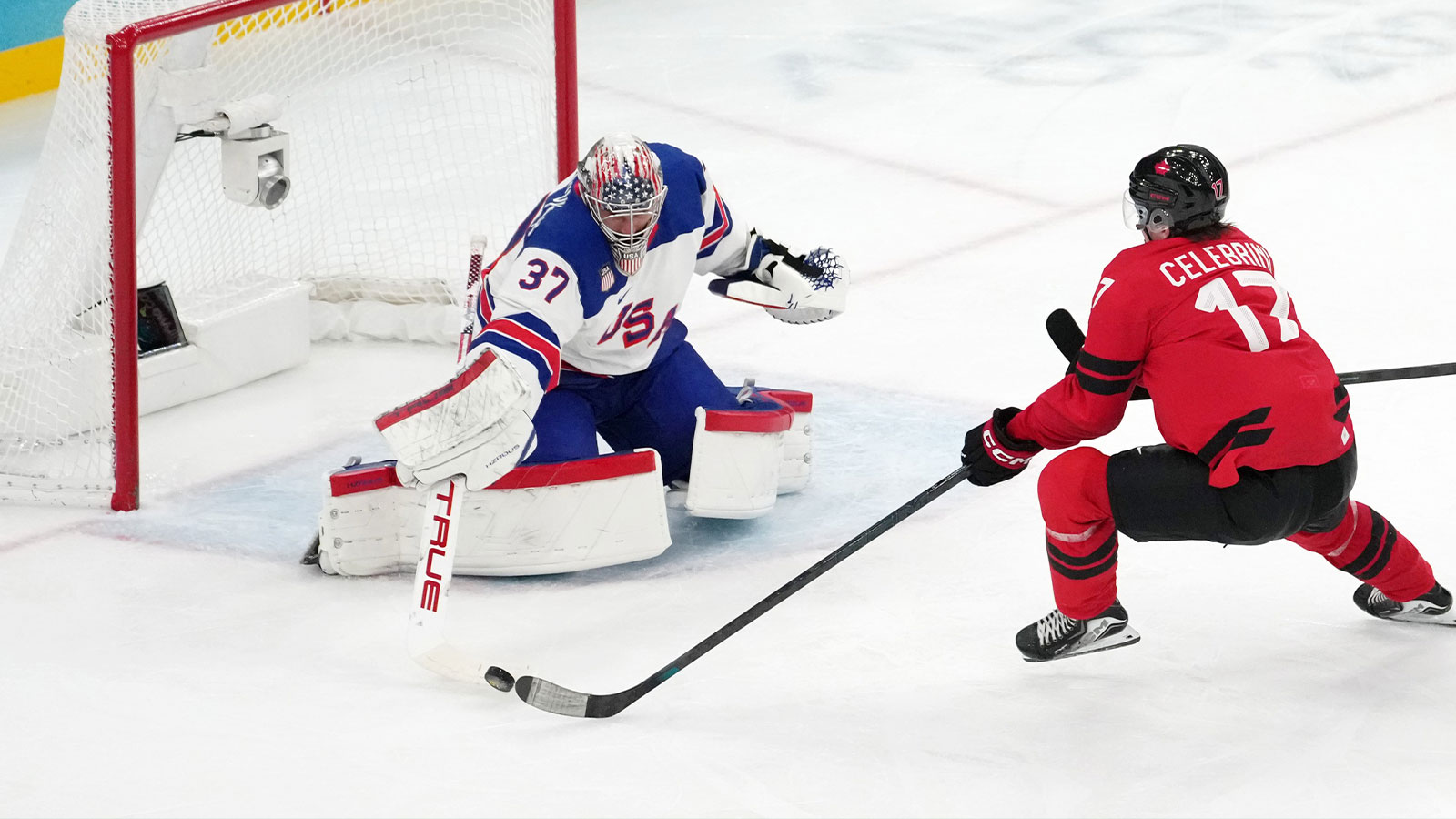 Connor Hellebuyck of the United States battles for the puck against Macklin Celebrini of Canada during the men's ice hockey gold medal game during the Milano Cortina 2026 Olympic Winter Games at Milano Santagiulia Ice Hockey Arena.