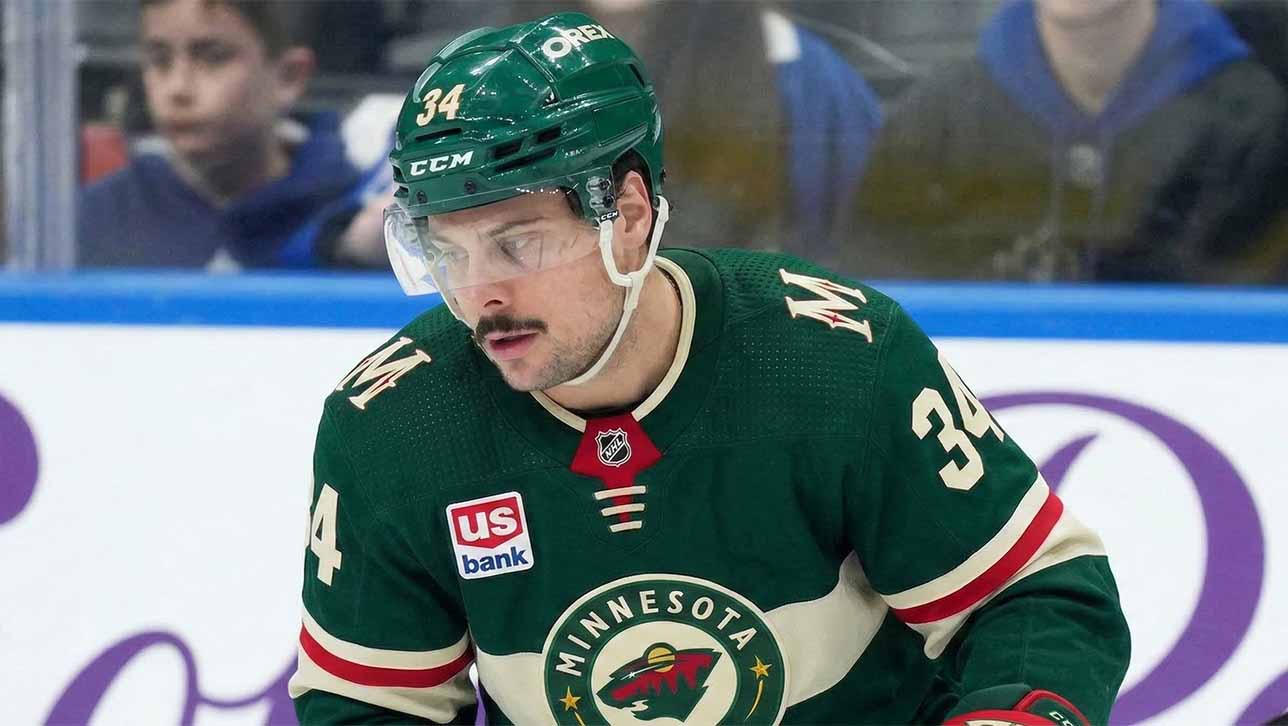 A close-up of Toronto Maple Leafs captain Auston Matthews (#34) in a Minnesota Wild jersey on the ice, appearing focused. Matthews is central to recent blockbuster NHL trade rumors linking him to the Wild.