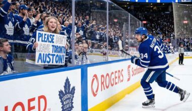 Toronto Maple Leafs fan behind glass at a hockey game holding a hand-drawn sign that says 'PLEASE DON'T LEAVE TORONTO AUSTON!' directed at Auston Matthews (#34) who is skating past on the ice.