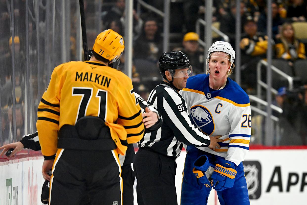 Rasmus Dahlin of the Buffalo Sabres and Evgeni Malkin of the Pittsburgh Penguins are separated by a referee during a hockey game.