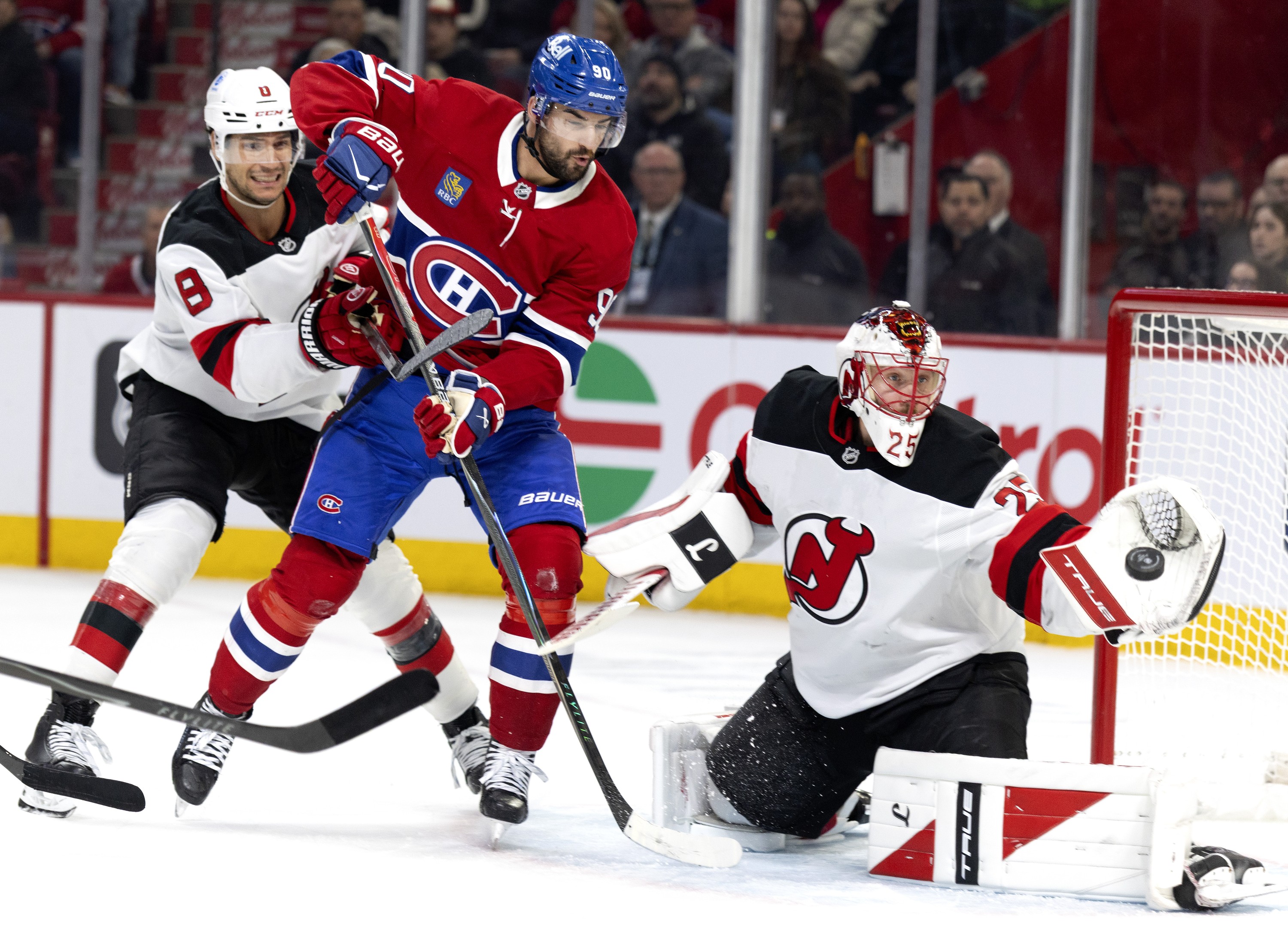 Montreal Canadiens centre Joe Veleno watches teammate Lane Hutson's shot go wide on New Jersey Devils goaltender Jacob Markstrom as Devils defenceman Johnathan Kovacevic tries to clear him from the crease.