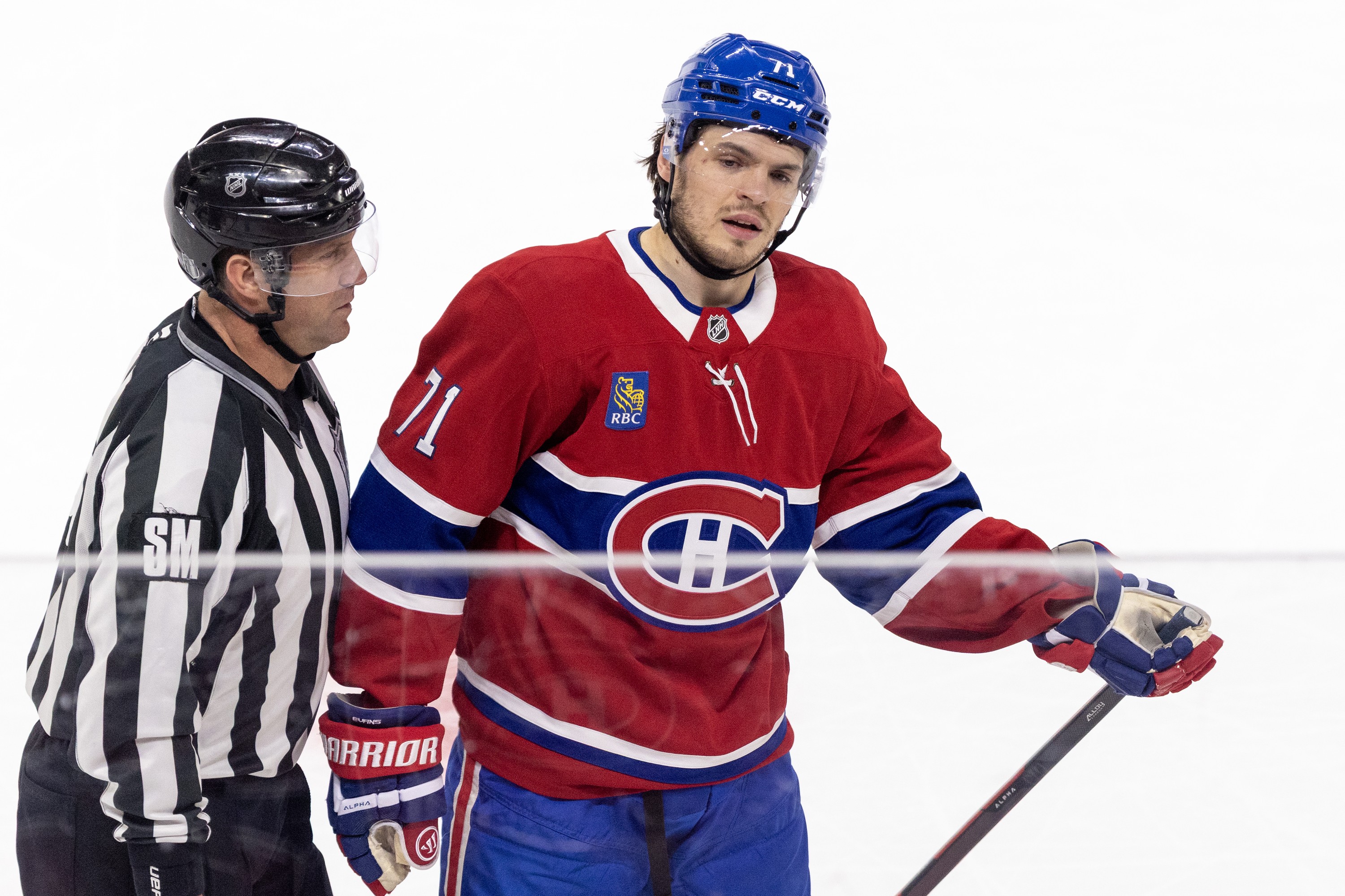 Montreal Canadiens' Jake Evans is escorted to the penalty box by a referee.