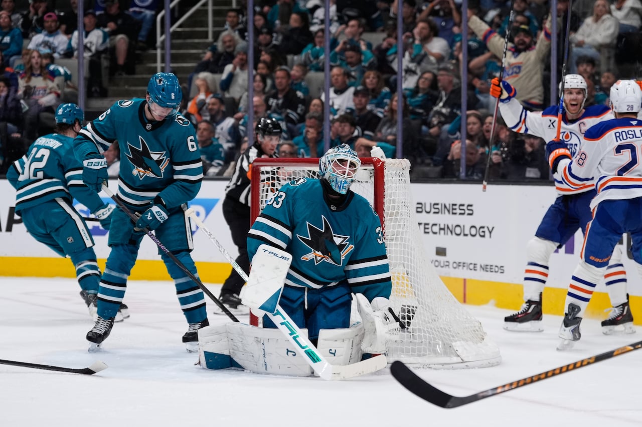 A hockey goaltender on the ice looks skyward, while two hockey players on the opposite team celebrate. 