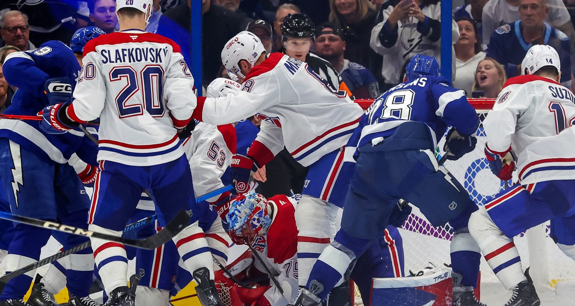 A bunch of Canadiens and Lightning players crowd around a Canadiens goalie bent over on the ice
