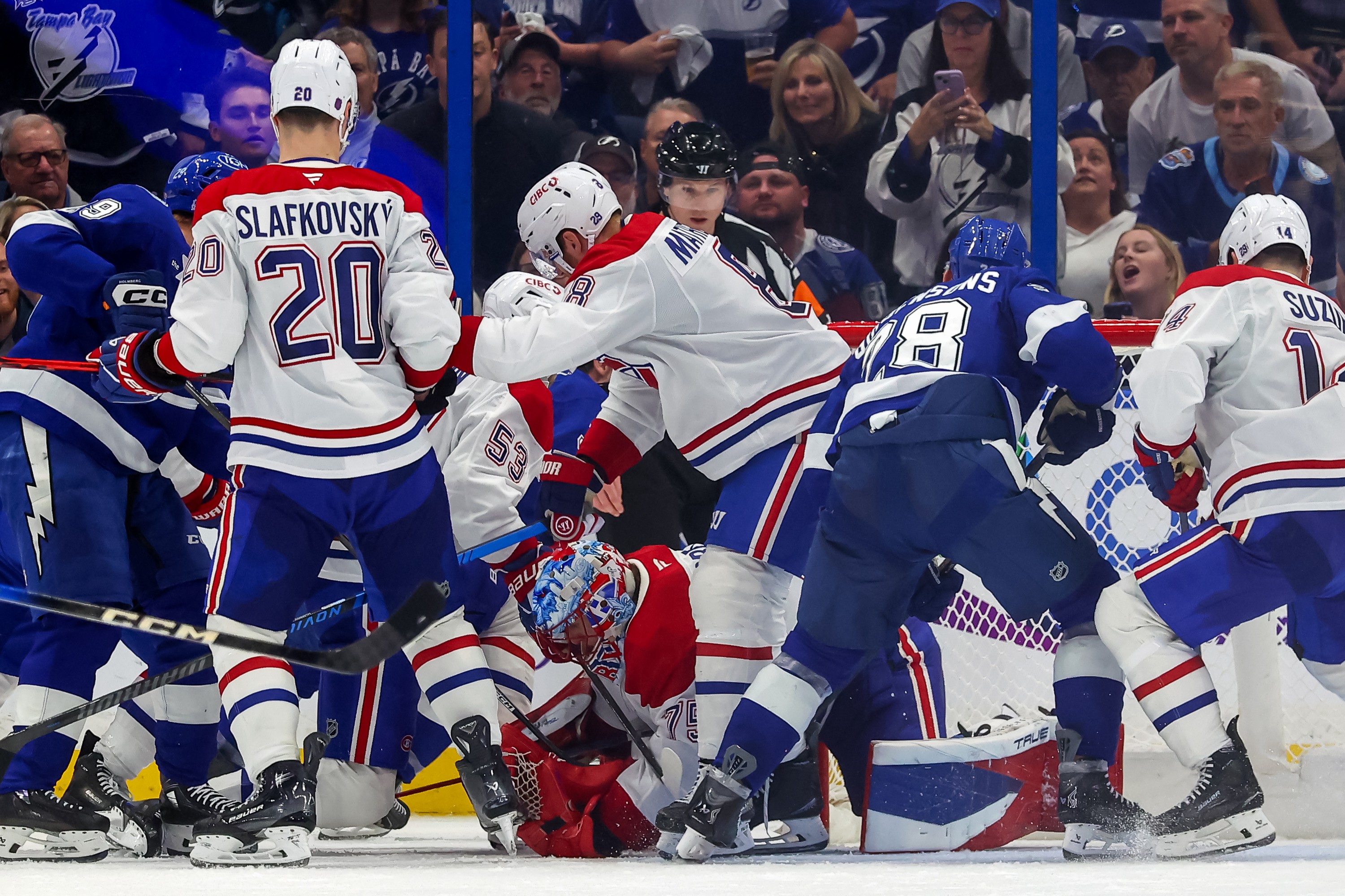 A bunch of Canadiens and Lightning players crowd around a Canadiens goalie bent over on the ice