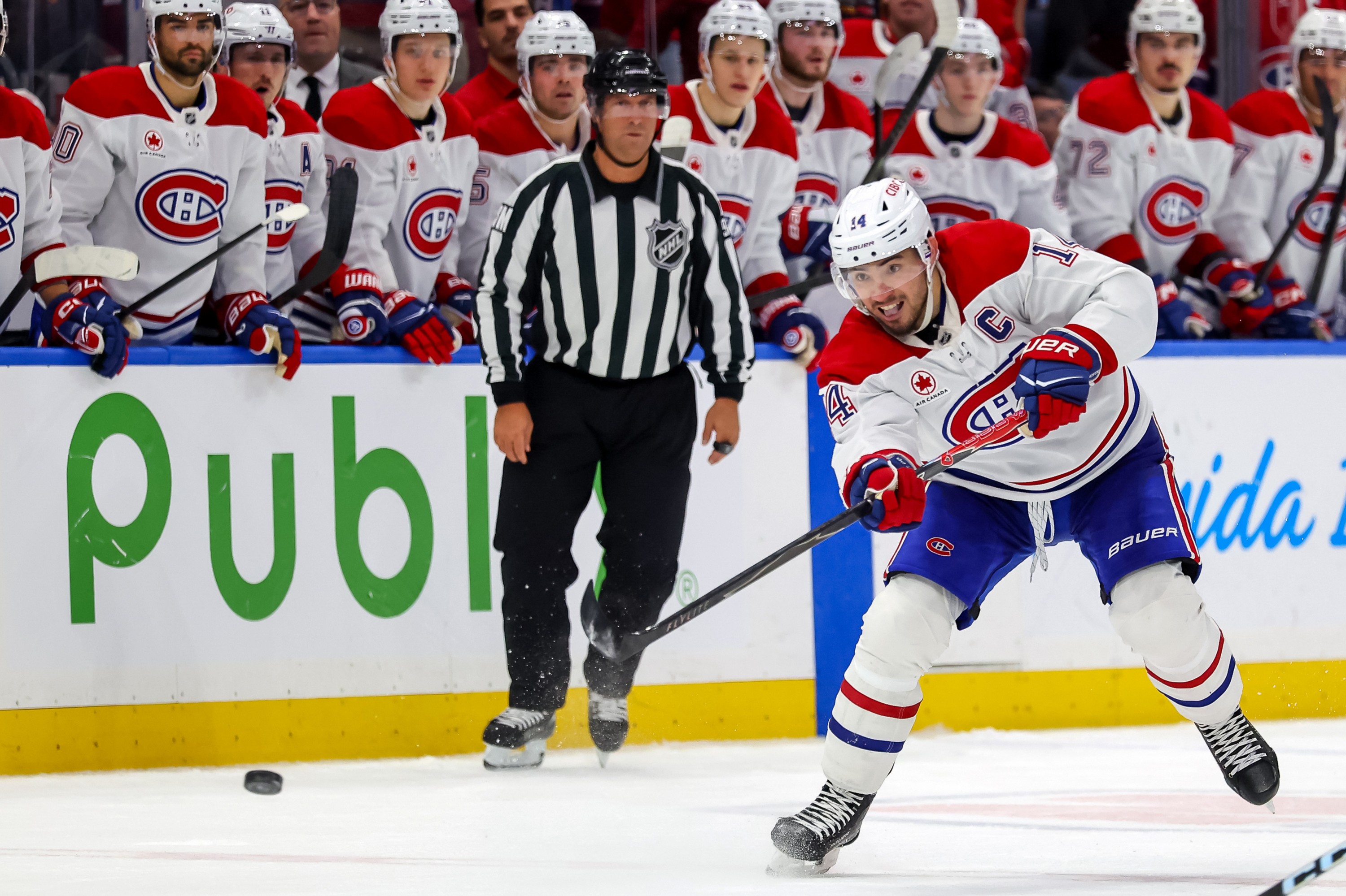 Nick Suzuki of the Montreal Canadiens shoots the puck down the ice while his teammates watch from the bench
