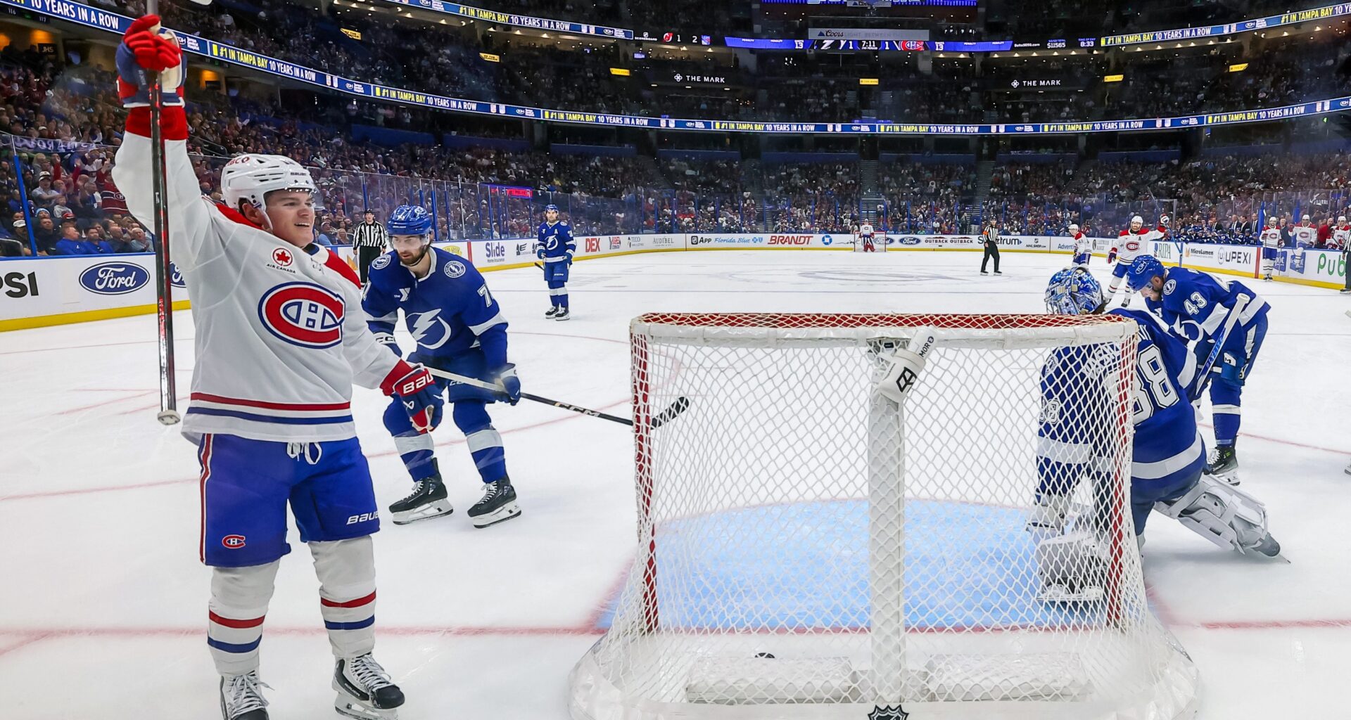Cole Caufield raises his arm in the air as he skates by the Tampa net, in a photo shot from behind the net