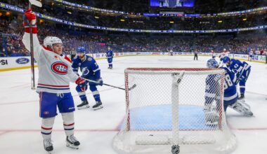 Cole Caufield raises his arm in the air as he skates by the Tampa net, in a photo shot from behind the net