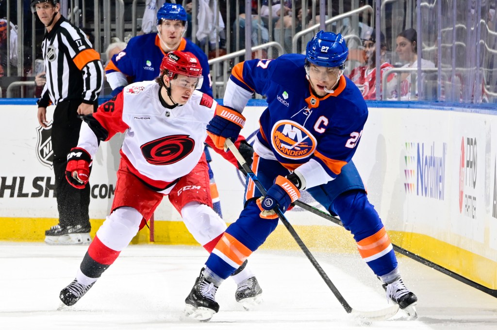 Hockey players Anders Lee (NY Islanders) and Felix Unger Sorum (Carolina Hurricanes) face off on the ice with a referee nearby.