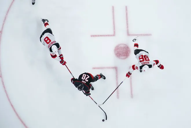 Mar 28, 2026; Raleigh, North Carolina, USA; Carolina Hurricanes center Sebastian Aho (20) skates with the puck between New Jersey Devils center Jack Hughes (86) and defenseman Johnathan Kovacevic (8) during the third period at Lenovo Center.