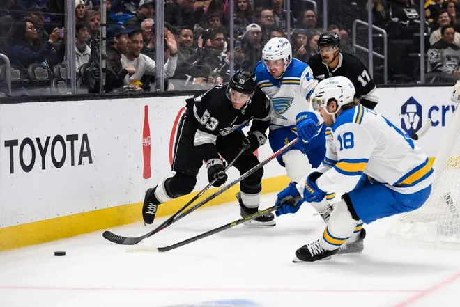 Apr 1, 2026; Los Angeles, California, USA; Los Angeles Kings right wing Jared Wright (53) tries to keep control of the puck while under pressure from St. Louis Blues center Robert Thomas (18) and defenseman Justin Holl (4) during the second period at Crypto.com Arena.