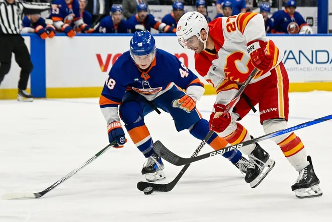 Mar 14, 2026; Elmont, New York, USA; Calgary Flames right wing Matt Coronato (27) skates with the puck defended by New York Islanders defenseman Matthew Schaefer (48) during the third period at UBS Arena.