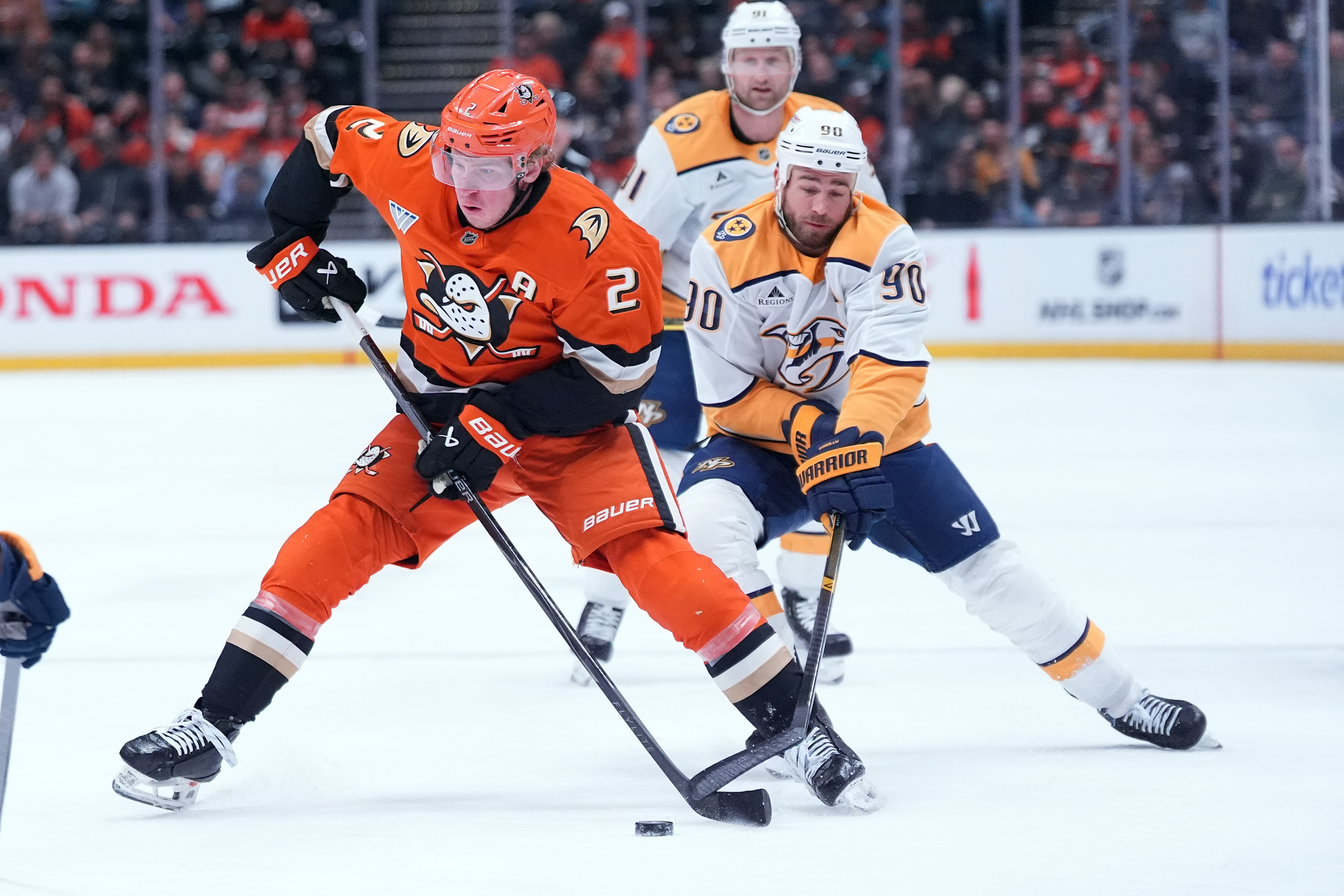 Ducks defenseman Jackson LaCombe, left, brings the puck across the...