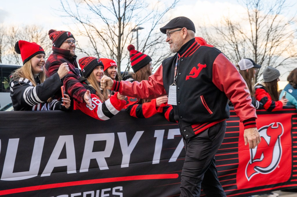 Man in a New Jersey Devils jacket fist-bumping fans behind a barrier.