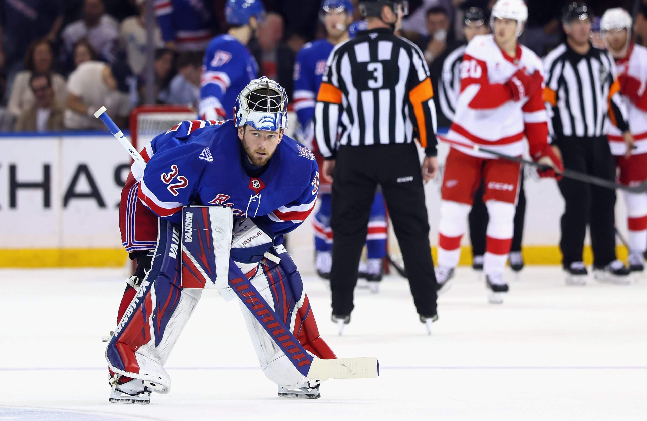 Jonathan Quick leans over with his mask up during a pause in play in a Rangers game, with players and referees in the background.