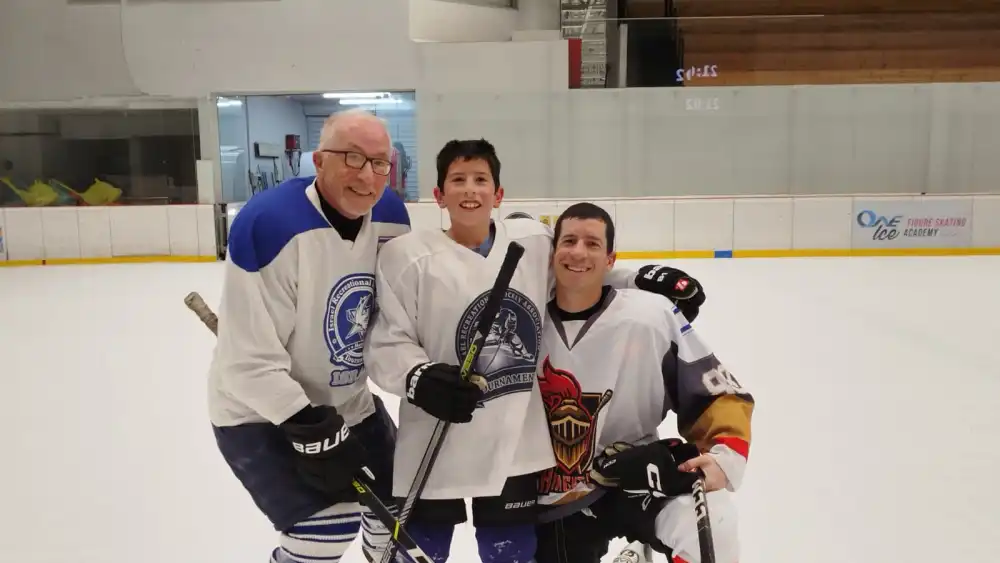 A grandfather, son and grandson wearing hockey jerseys at an ice rink.