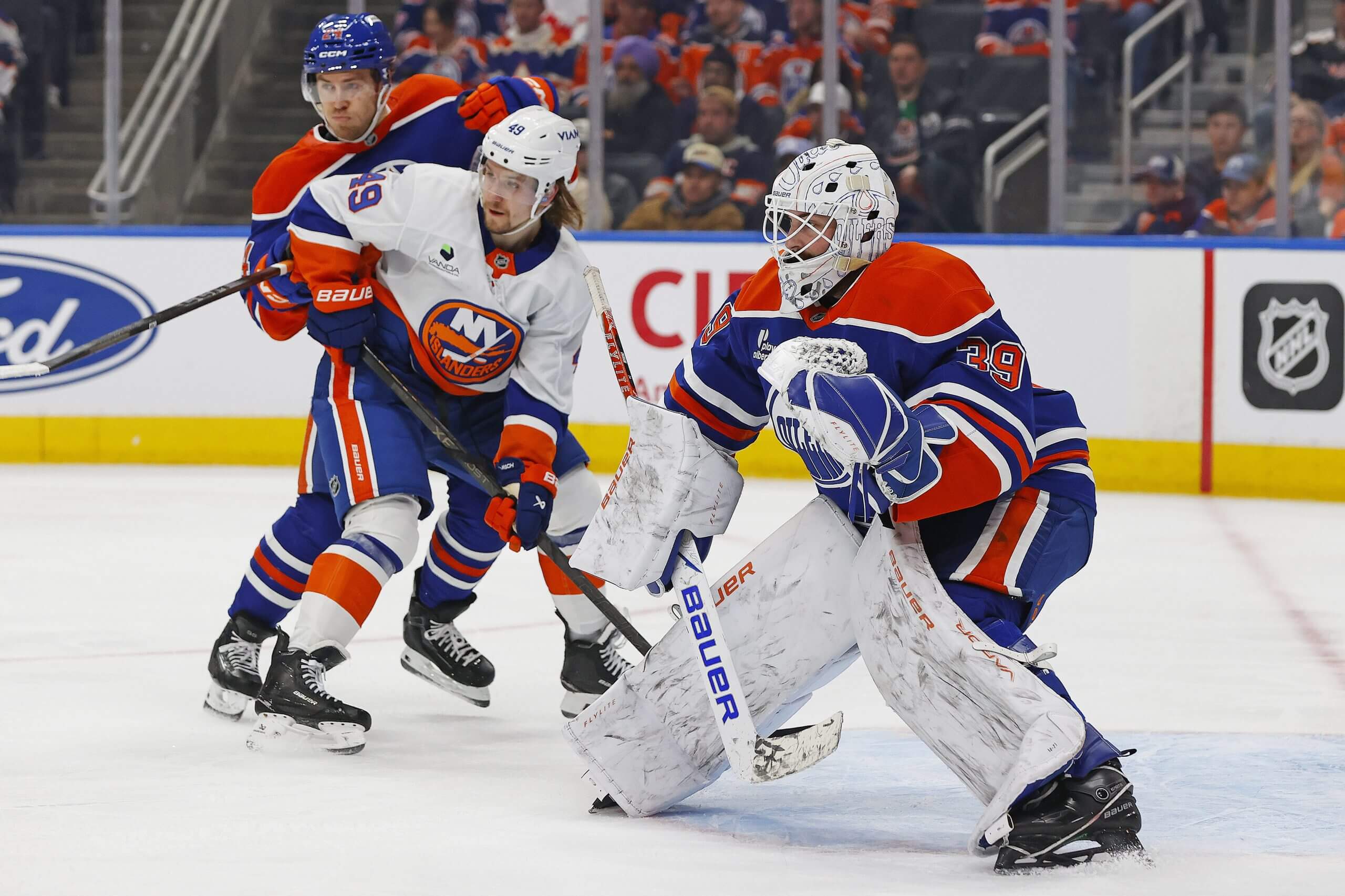 Connor Ingram squares up to a shot with the Oilers, with a teammate and an Islanders player fighting for position near the net.