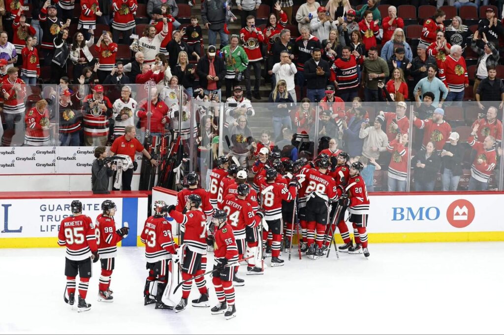 Blackhawks players celebrate on the ice while fans cheer from the stands.