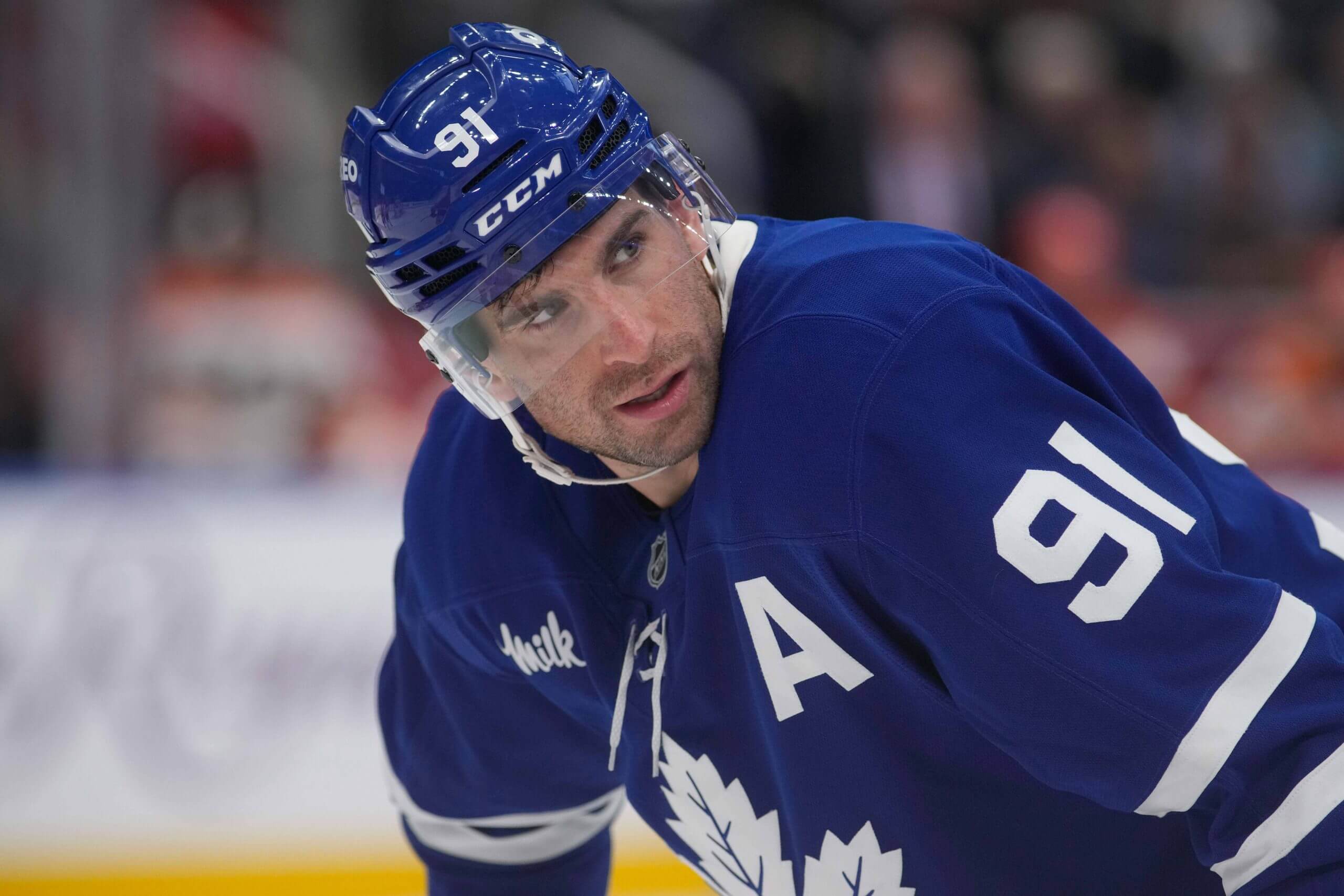 John Tavares, in a blue helmet and jersey, leans over on the ice while looking over his left shoulder.
