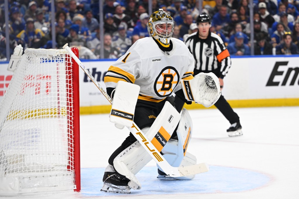 Boston Bruins goalie Jeremy Swayman in his white, black, and gold uniform guarding the net during a hockey game.