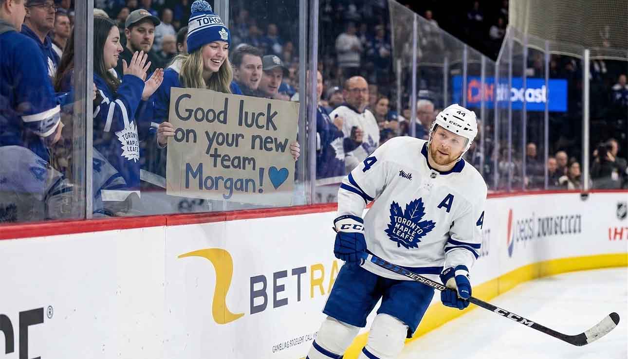 Toronto Maple Leafs defenseman Morgan Rielly skates past a young fan holding a cardboard sign that reads "Good luck on your new team Morgan!" amid persistent trade rumors.