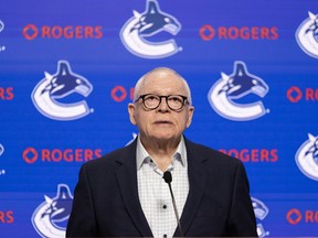 Jim Rutherford stands at a podium in front of a blue Canucks banner