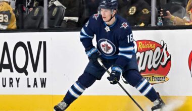 A close-up action shot on ice of hockey player Pavel Dorofeyev, featuring his likeness and low-crouched pose, now in a navy blue Winnipeg Jets home uniform and helmet with number 16, controlling a puck with his stick and creating ice spray.