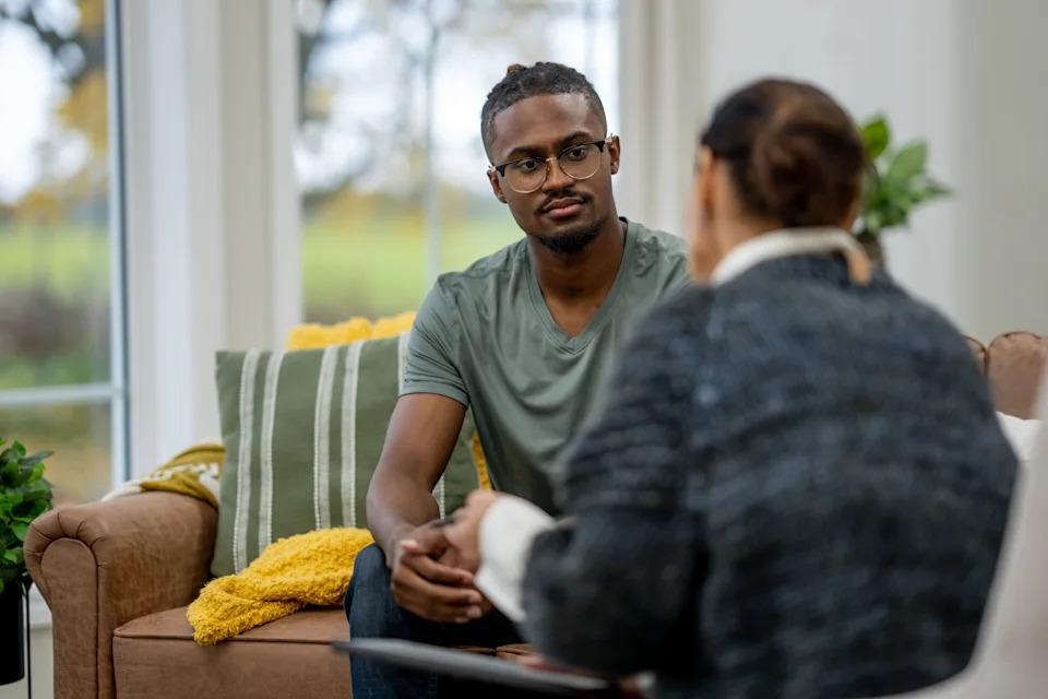 A man attentively listens to a counselor during a therapy session, promoting mental health awareness and support in a cozy setting