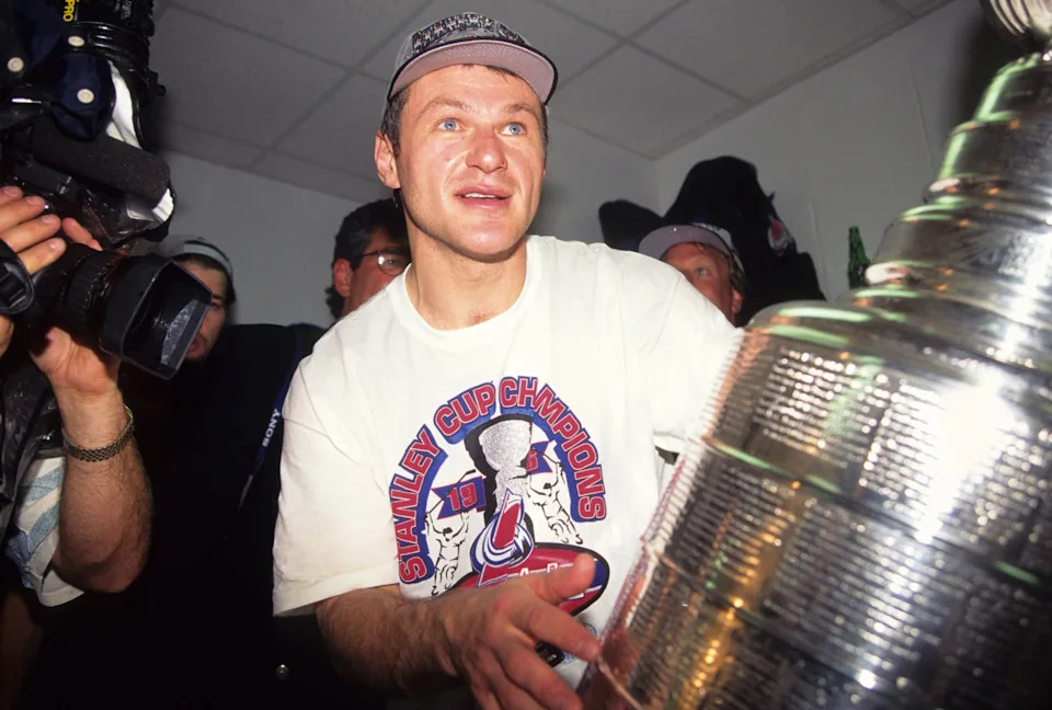 Person wearing a "Stanley Cup Champions" shirt and cap, holding the Stanley Cup trophy in a celebratory setting with cameras around