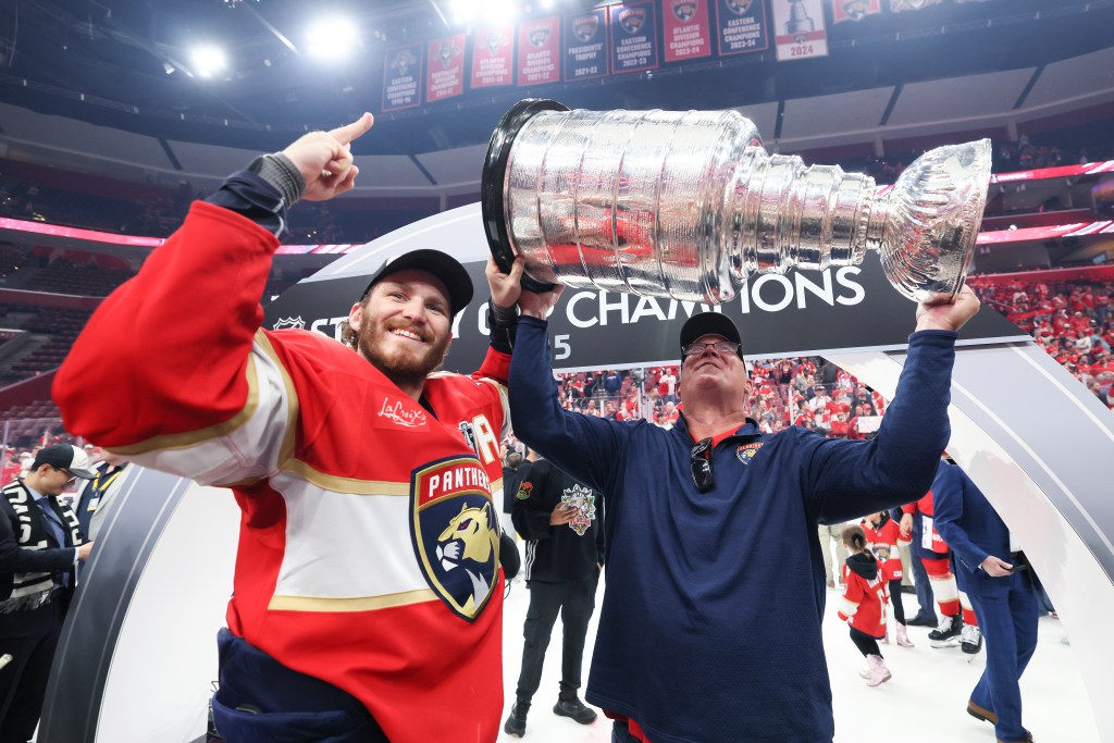 A hockey player and a team official raising the Stanley Cup in celebration after winning the 2025 Stanley Cup Final.