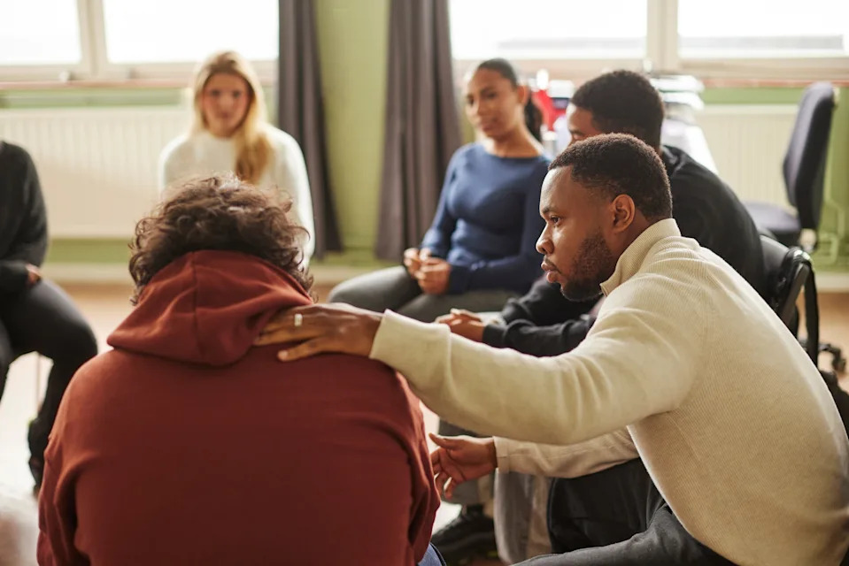 A group therapy session with diverse individuals seated in a circle, one person comforting another with a hand on their back