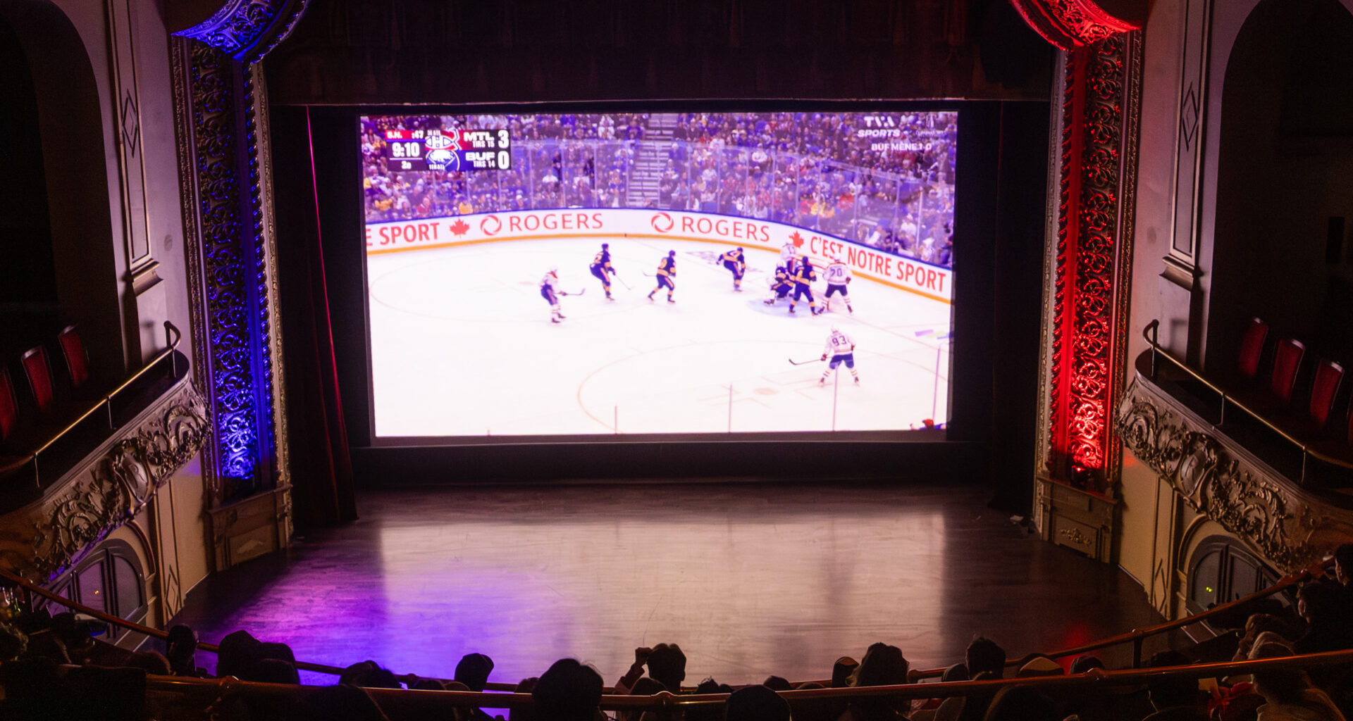 People sitting in movie theatre watching hockey game on big screen.