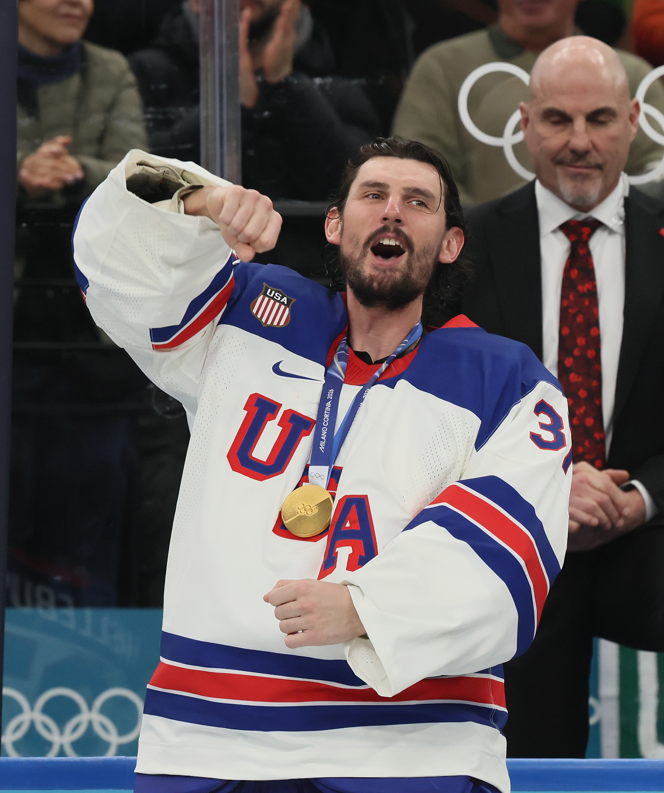 A male hockey player from the USA team celebrating with a gold medal around his neck.