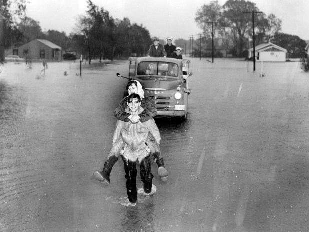 B. A. Mylosh carries his wife to a dry spot on 119th Street after their home was flooded at 118th Street and Pulaski Road in Alsip on Oct. 10, 1954. (Dan Tortorell / Chicago Tribune) photo published October 11, 1954