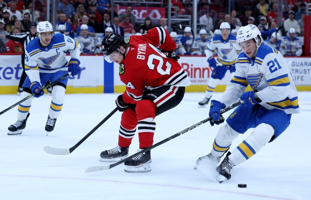 Chicago Blackhawks defenseman Bowen Byram (24) and St. Louis Blues right wing Jimmy Snuggerud (21) battle in the first period of the Blackhawks home opener at the United Center in Chicago on Oct. 6, 2026. (Chris Sweda/Chicago Tribune)