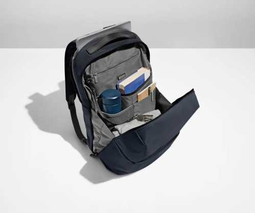 A navy backpack open to reveal a laptop, notebooks, a water bottle, and various accessories inside.