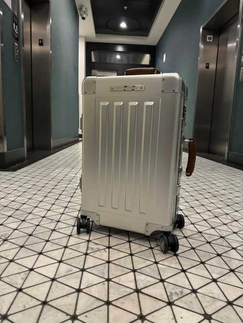 A silver suitcase on wheels in a hotel hallway with elevators in the background.