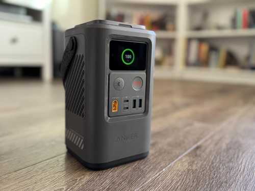 A portable power station with a digital display, USB ports, and a sleek design, placed on a wooden floor.