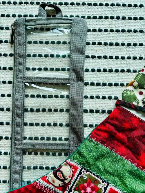 A gray organizer with clear pockets next to a colorful quilt featuring festive patterns on a striped rug.