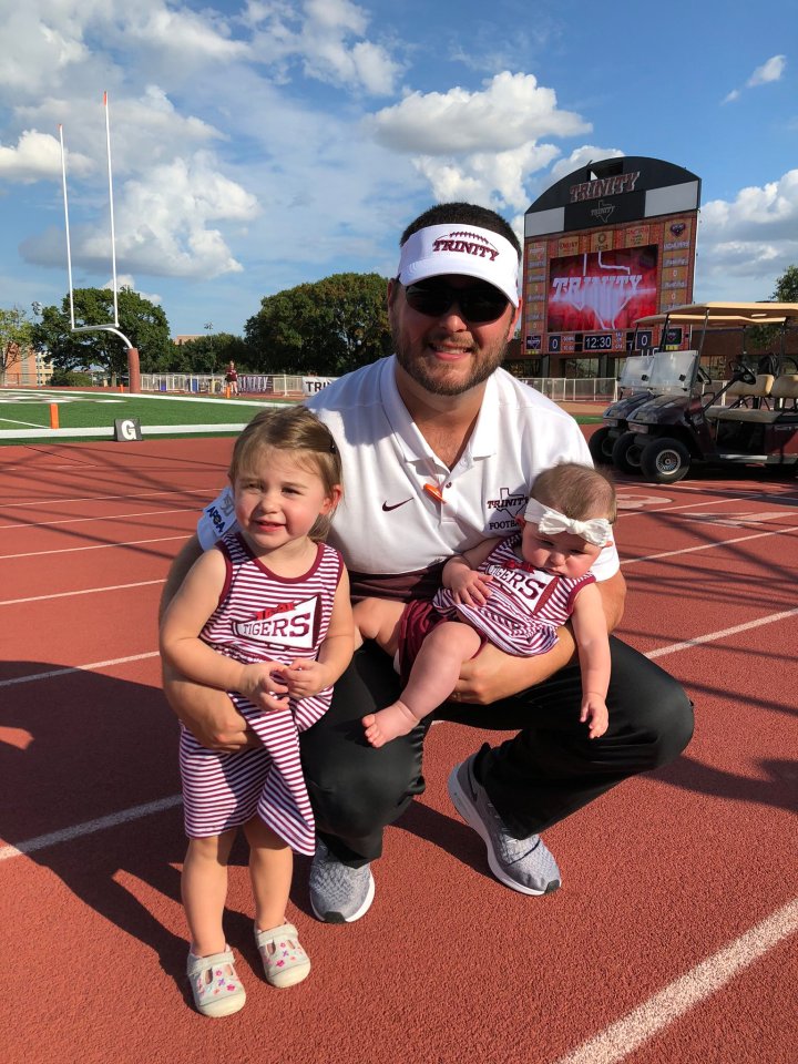 A man holding his two young daughters at a football field.