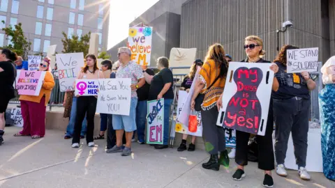 Reuters Protesters in front of courthouse hold signs showing support for EM that read "We believe her", "Justice for EM" and "My dress is not a yes"