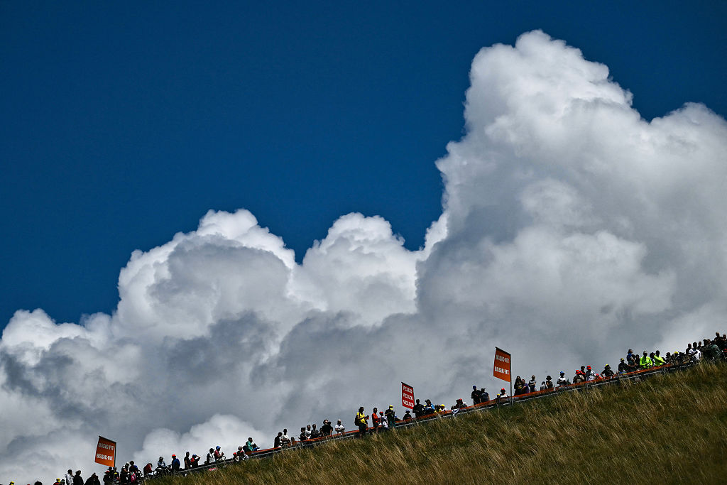 Clouds dominate the skyline as spectators line the race route on a steep incline in the ascent of Col du Glandon during the 18th stage of the 112th edition of the Tour de France cycling race, 171.5 km between Vif and Courchevel Col de la Loze, in the Alps, southeastern France, on July 24, 2025. (Photo by Marco BERTORELLO / AFP)