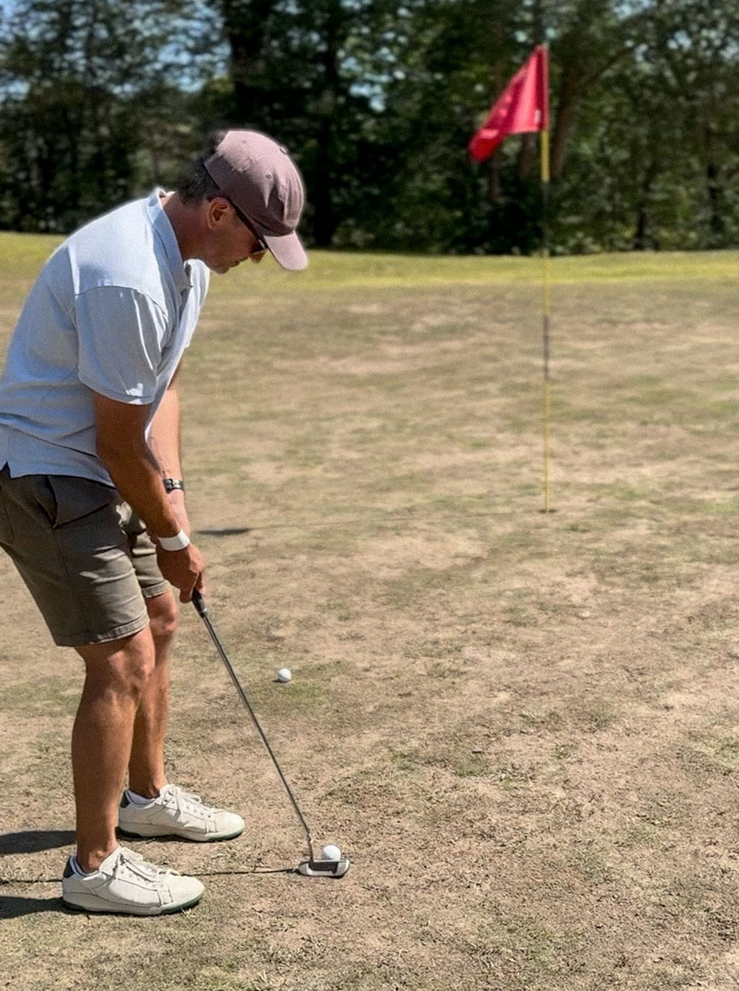 A golfer lining up his shot near a hole on a hole with mostly dirt around the hole.
